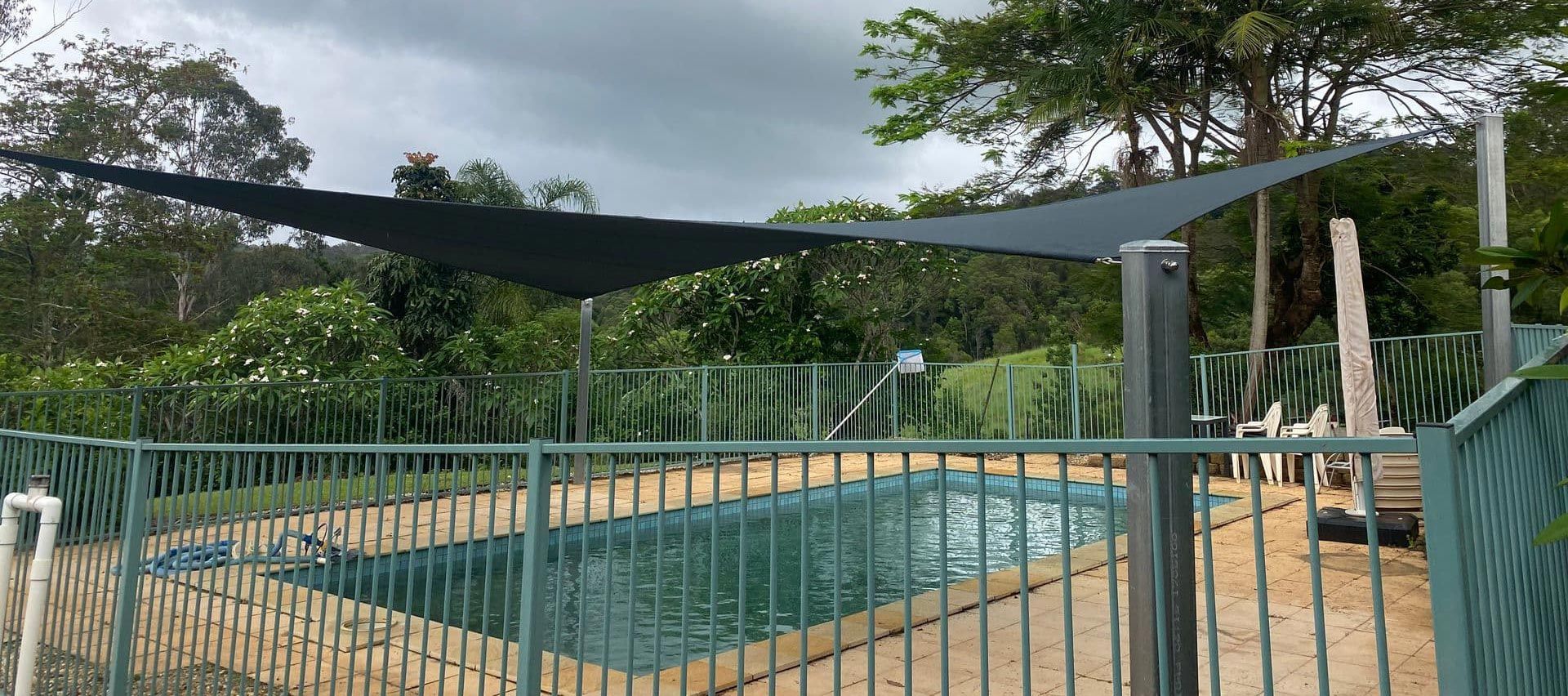 Twin charcoal shade sails installed over a fenced backyard pool